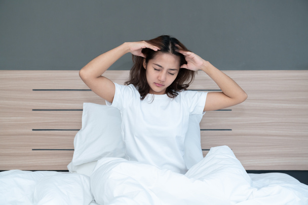 Mladé asijské ženy ležící v posteli drží hlavu, které mají silné bolesti hlavy možná migrény v dopoledních hodinách na posteli - Fotografie, Obrázek