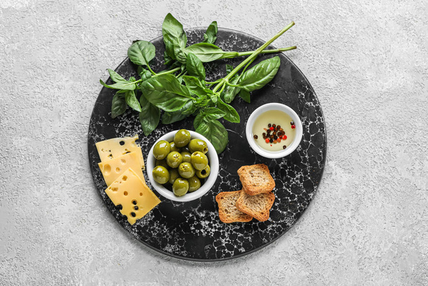 Board with bowl of tasty green olives, oil, cheese, crackers and basil on light background - Fotoğraf, Görsel