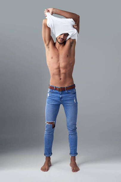 All he needs is jeans. Studio shot of a handsome young man undressing against a grey background - Valokuva, kuva