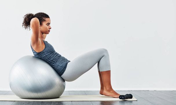 Every workout is a step closer to your goal. a young woman exercising using a fitness ball - Foto, Bild