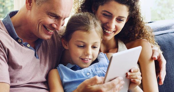 Family time done in the digital age. a cute little girl using a digital tablet with her mother and father on the sofa at home - Foto, imagen