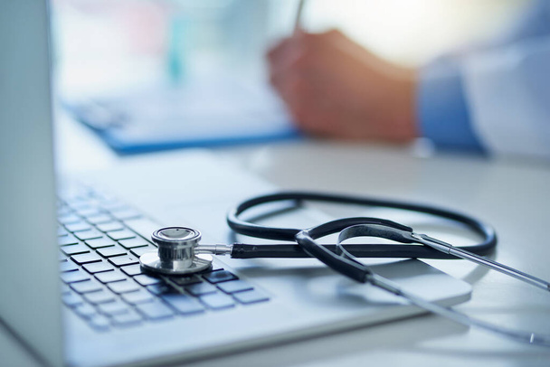 Technology - the greatest tool for medical advancement. Closeup shot of a stethoscope resting on a laptop with an unrecognizable doctor working in the background - Foto, Imagem