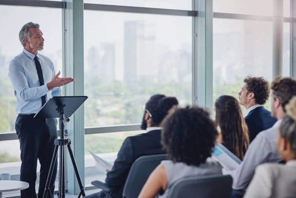 Hes got a wealth of experience to share. High angle shot of a handsome mature male speaker addressing a group of businesspeople during a seminar in the conference room - Photo, Image