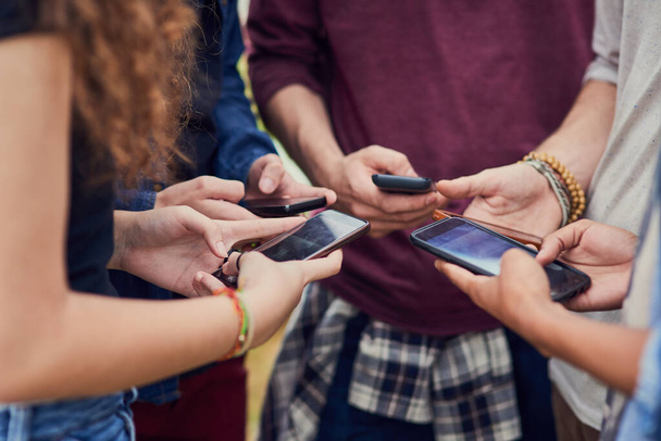 Життя в епоху технологій. група молодих невпізнаваних людей, що стоять в колі під час перегляду на своїх мобільних телефонах зовні протягом дня
 - Фото, зображення