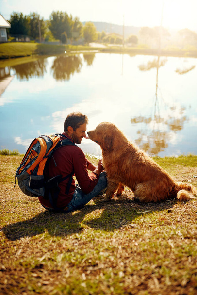 Youre such a good boy. Full length shot of a handsome young man and his dog sitting by a lake in the park - Foto, imagen