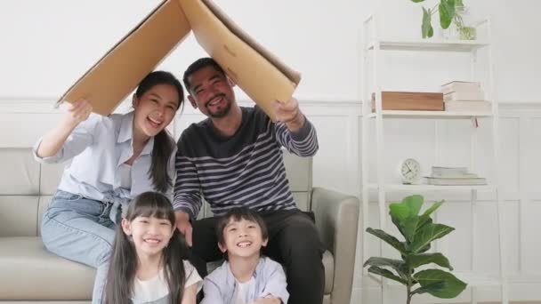Азійська тайська сім'я, дорослий тато, мама і маленькі діти радісно бавилися в білій вітальні, будували картонний паперовий будинок з уявою, прекрасними вихідними і свіжим домашнім життям.. - Кадри, відео