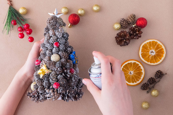 Ψυχραιμία Βήμα 5. Φτιάχνω ένα διακοσμητικό χριστουγεννιάτικο δέντρο από κουκουνάρια. Top view υλικά για την κατασκευή διακοσμητικών παιχνιδιών, τεχνητό χιόνι χρησιμοποιείται. - Φωτογραφία, εικόνα
