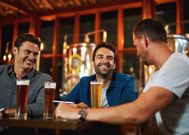 Good company, good times. a group of young friends seated at a table together while enjoying a beer inside a bar - Foto, imagen