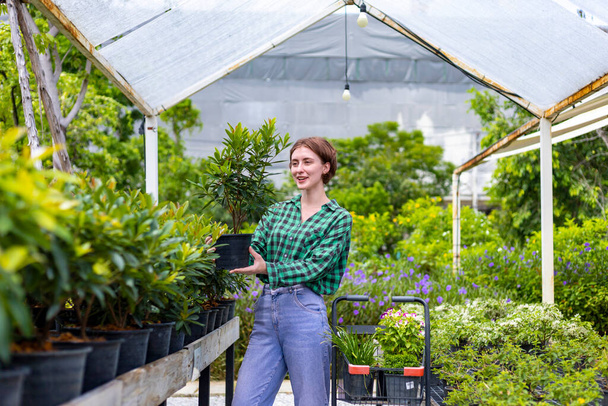 Young caucasian customer is choosing exotic plant from the local garden center nursery with shopping cart full of summer plant for weekend gardening and outdoor concept - Foto, Imagem