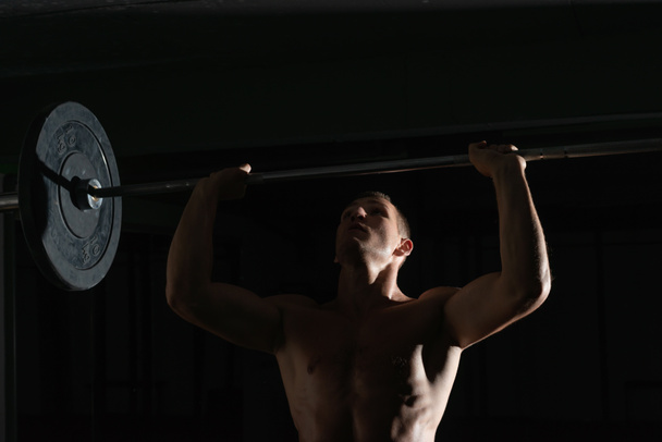 Close up silhouette di un bodybuilder facendo spallaccio spallina barbel in una palestra mentre flette il suo ritratto muscoli. - Foto, immagini