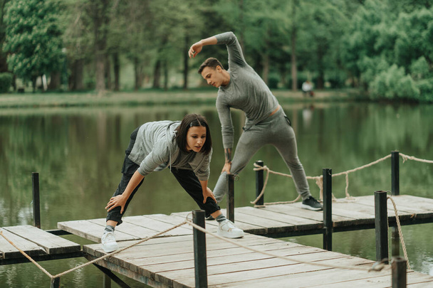 Close up of strong couple working out on the bridge near the lake in the park - Foto, afbeelding