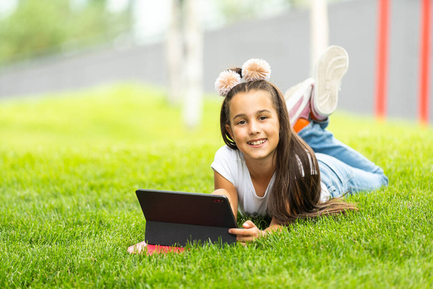 Little girl sitting on grass and playing tablet pc. - Fotoğraf, Görsel