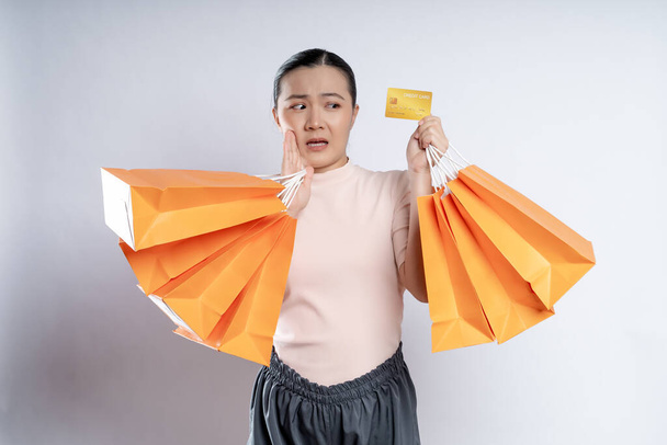 Азійська жінка винна в тому, що нервує, тримаючи більше сумок і кредитну картку ізольованою над білим фоном.. - Фото, зображення