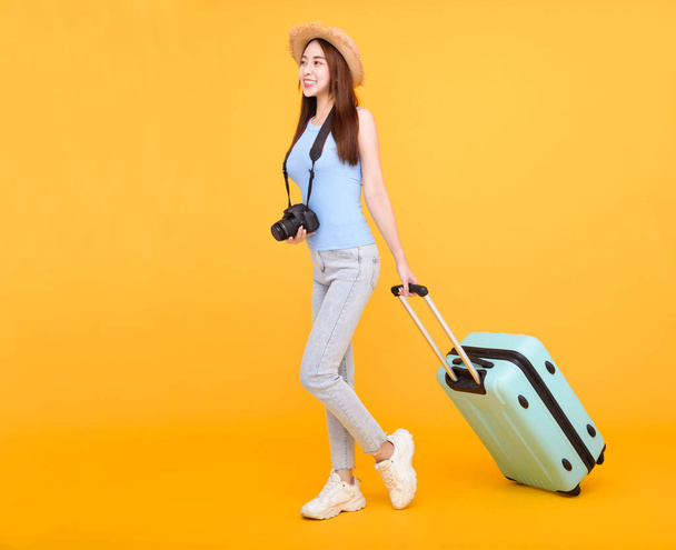 Ευτυχισμένη νεαρή γυναίκα με αποσκευές και κάμερα απομονωμένη σε κίτρινο φόντο, καλοκαίρι, ταξιδιωτική έννοια. - Φωτογραφία, εικόνα