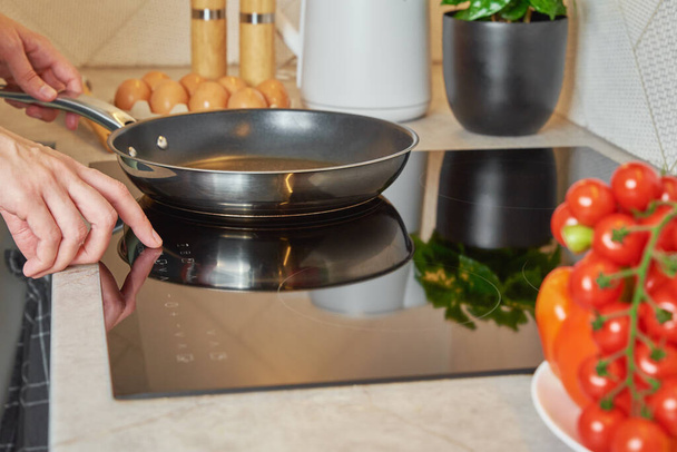 Modernes Küchengerät, Frau schaltet Induktionsherd mit Stahlpfanne ein, Finger berühren Sensor-Taste auf Induktion oder Elektroherd - Foto, Bild
