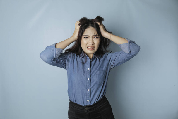 Portrait of young Asian woman isolated by blue background feeling frustrated with helpless face expression. - Foto, Imagen