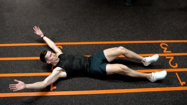 Gym abs workout exercise. Sportsman man in sportswear doing raised-leg sit-up and clap exercises on gym floor, exercising. athletic fit man in the gym workout - Footage, Video