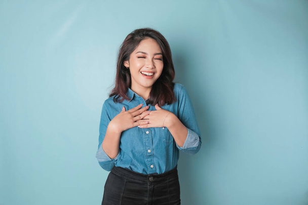 Happy mindful thankful young woman holding hands on chest smiling isolated on blue background feeling no stress, gratitude, mental health balance, peace of mind concept. - 写真・画像