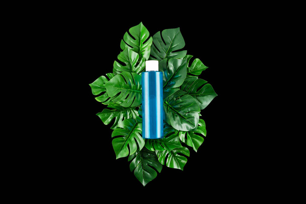 Blue Bottle with tropical monstera leaf on isolated black background close up. Brand packaging mockup. Moisturized, skincare beauty micellar water or serum. Natural herbal cosmetics concept - Foto, afbeelding