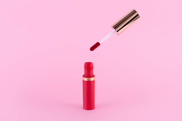 Lipstick and applicator wand on pastel pink background. Liquid lip stick red lip gloss open tube. Makeup cosmetic product. Top view, flat lay, copy space - Fotografie, Obrázek