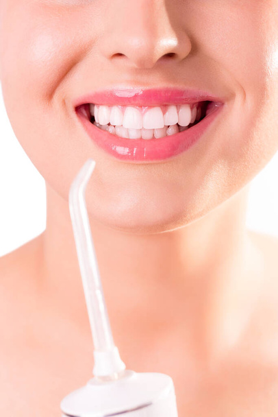 Γυναίκα με τέλειο λευκό χαμόγελο χρησιμοποιώντας φορητό οδοντικό νήμα νερού ή πόσιμο αρδευόμενο. Οδοντιατρική φροντίδα. Ευτυχισμένο πρόσωπο σε νεαρή γυναίκα. Απομονωμένα σε λευκό φόντο - Φωτογραφία, εικόνα