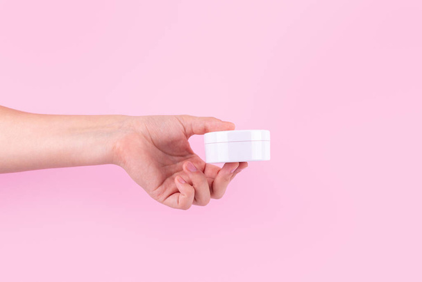Female hand holding unbranded plastic tube. Flacon for cream, toiletry. Bottle for professional cosmetics product. Skincare and beauty concept. Mockup, copy space. Isolated on pink - Photo, Image