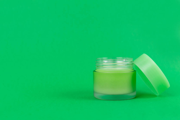 Opened green jar with cream on isolated green background close up. Brand packaging mockup. Aromatic oil, skincare beauty product, cream or serum. Natural herbal cosmetics concept - Photo, Image