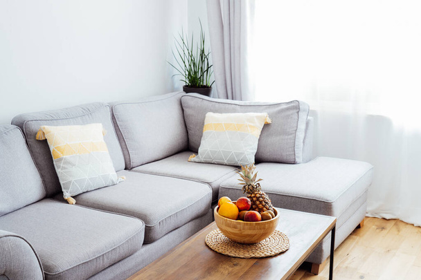 Stylish and modern scandinavian interior of open space living room with bamboo bowl with fruits on the coffee table, gray couch sofa, and many green plants. Biophilia. Open space home interior design. - Zdjęcie, obraz