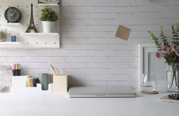 Δημιουργικός χώρος εργασίας με laptop, κορνίζα, γλάστρα και γραφική ύλη σε λευκό τραπέζι. - Φωτογραφία, εικόνα