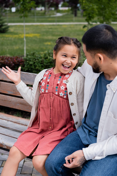 Excited asian girl talking to father on bench in park  - Fotoğraf, Görsel