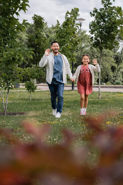 Positive asian parent and kid waving hands in summer park  - Photo, Image