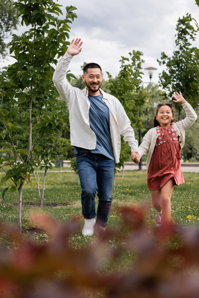 Happy asian father and child waving hands while running in park  - Foto, immagini