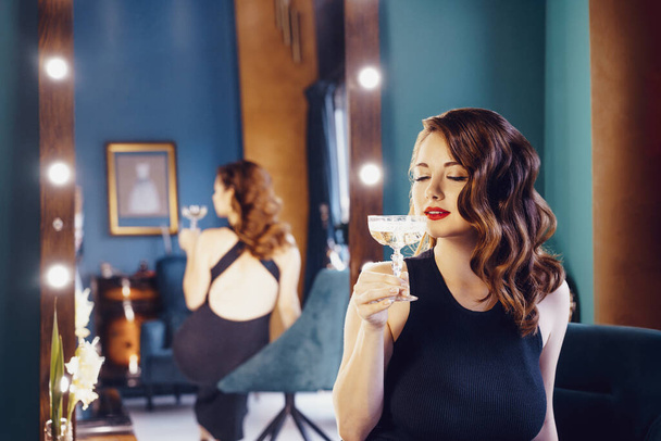 Posh elegant woman in evening dress with a glass of champagne in the luxury dressing room interior. Celebrity, superstar lifestyle. Party, drinks, holidays and celebration concept. Selective focus - Photo, image