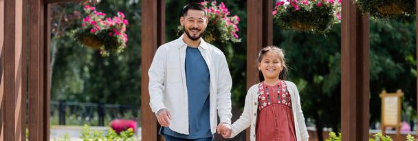 Smiling asian parent and child holding hands while walking in park, banner  - Foto, Imagen