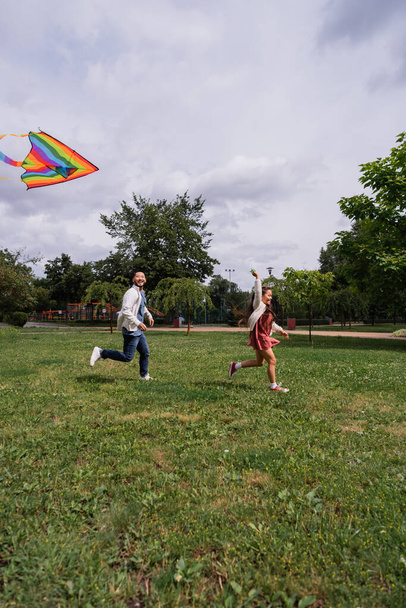 Positive asian man running near daughter with flying kite in park  - Foto, immagini