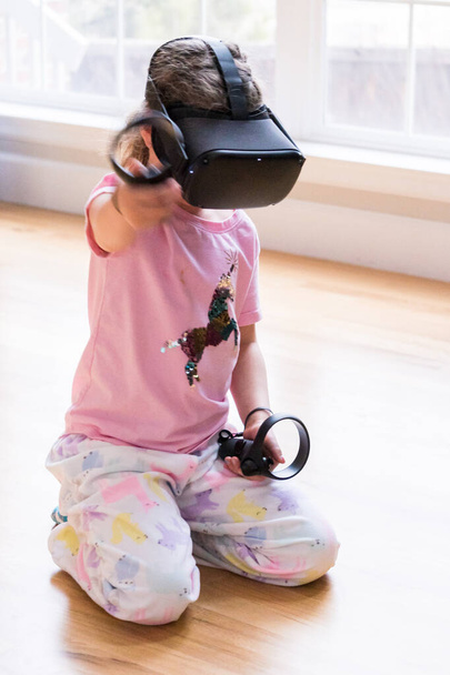 Μικρό κορίτσι που παίζει παιχνίδι εικονικής πραγματικότητας στο σαλόνι, - Φωτογραφία, εικόνα