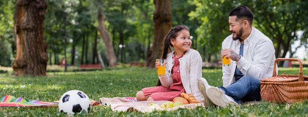 Asian child holding orange juice near food and dad in summer park, banner  - Photo, Image