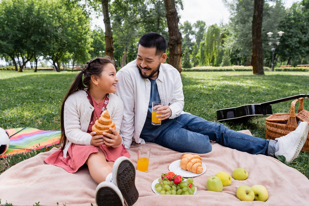 Asian family holding orange juice and croissant during picnic in park  - Fotó, kép