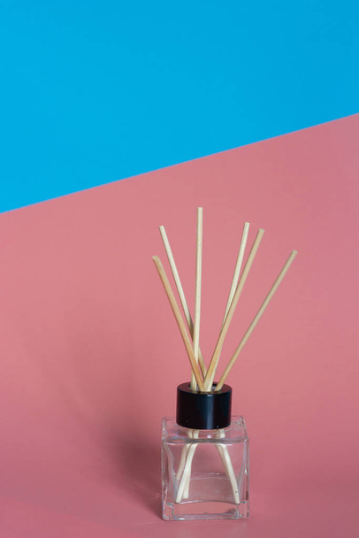 Home perfume bottle with perfume soaked incense sticks stands on blue and pink - Fotó, kép