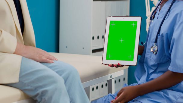 Medical nurse and patient looking at greenscreen on tablet, having appointment in cabinet. Specialist and elder woman analyzing blank chromakey display with isolated copyspace and mockup template. - Photo, Image