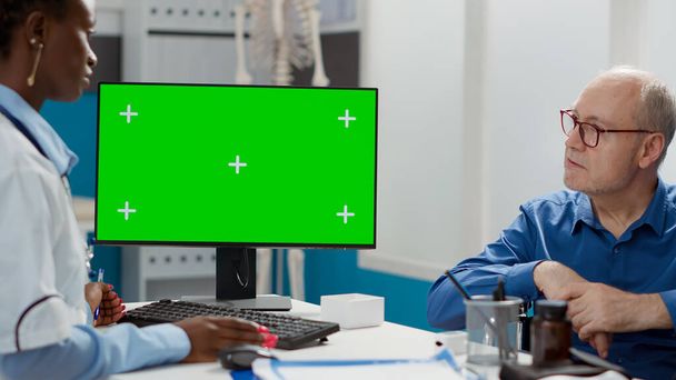 Physician and elderly man in wheelchair analyzing greenscreen in cabinet. Medic and patient with physical disability using isolated chromakey copyspace with blank mockup template. - 写真・画像
