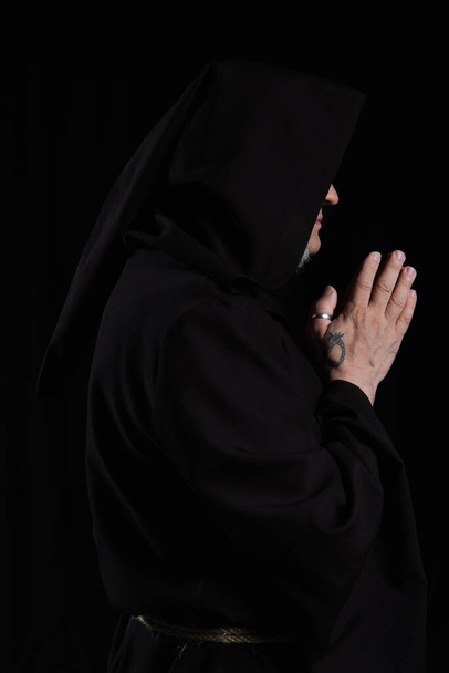 widok z boku wytatuowanego księdza z przysłoniętą twarzą modlący się odizolowany na czarno - Zdjęcie, obraz
