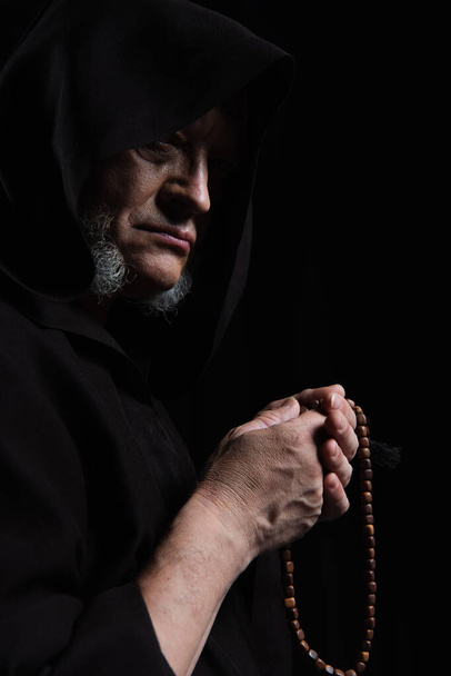 medieval monk in hood holding rosary isolated on black - Photo, Image