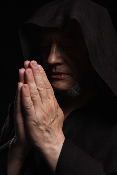 medieval monk with closed eyes and praying hands isolated on black - Foto, Imagen