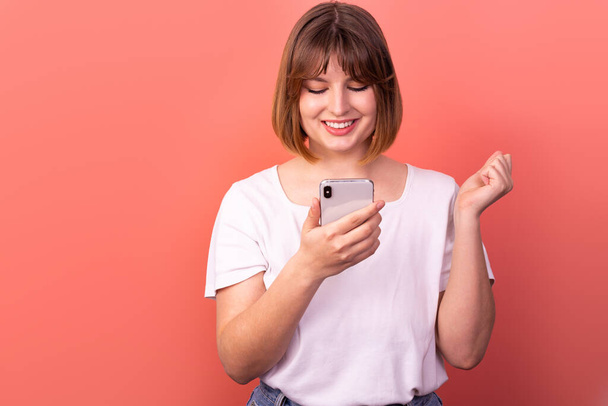 Portrait of a lovely amazed cheerful brown-haired woman using a 5g phone device as a reaction of delight and great joy, isolated on a pink pastel background. The concept of happiness. - Photo, Image