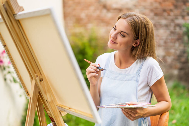 Woman enjoys painting on canvas outdoor. - 写真・画像