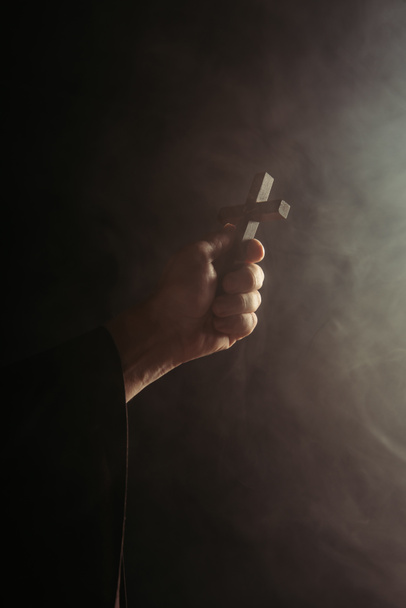 visão parcial de monge com cruz santa na mão sobre fundo preto com fumaça - Foto, Imagem