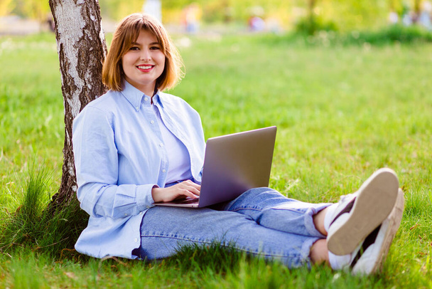 Photo portrait of pretty young woman smiling teeth sitting in green park working on laptop smiling - Foto, Bild