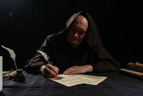 medieval abbot writing chronicle on parchment near inkpot isolated on black - Photo, Image