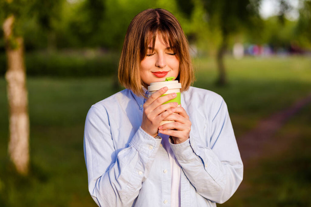 Photo portrait of girl holding bamboo cup smile and happy outdoors, smell tasty coffee in green park - Foto, Imagen